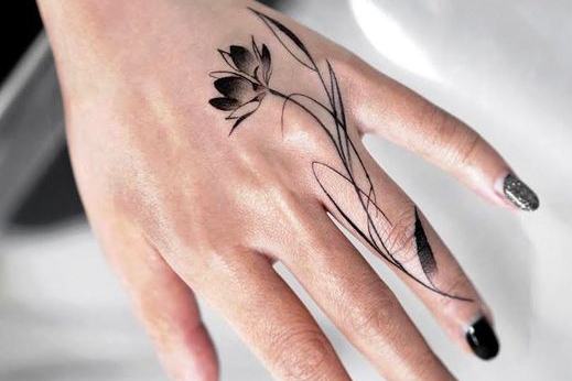 Jemné, minimalistické květinové tetování v blackwork/fine line stylu na hřbetu ruky; 