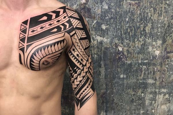 Velká tribal kompozice s výraznými černými plochami a negativním prostorem přes rameno, horní hrudník a paži; geometrické linie plynule kopírují anatomii.