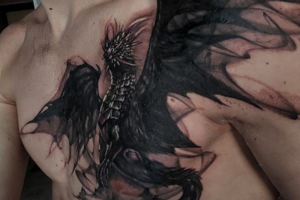 Blackwork tetování evropského draka s roztaženými křídly na hrudi a přes rameno; detailní šupiny, tmavé stínování a kompozice přirozeně kopírující anatomii.