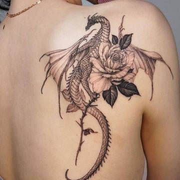 Blackwork tetování evropského draka s roztaženými křídly propleteného s velkou růží na horní části zad (lopatka)