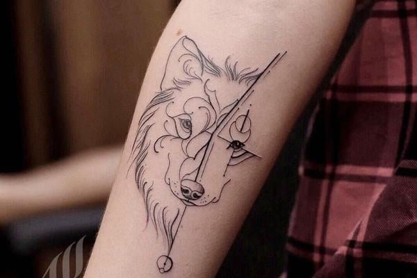 Jemné linework tetování vlčí hlavy s geometrickými prvky na vnitřním předloktí; čisté černé linie, moderní a čitelné.