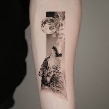 Vnitřní předloktí s černošedým realistickým tetováním vlka vyjícího k úplňku; motiv je zasazen do úzkého vertikálního panelu s dotwork stínováním a čistými liniemi.