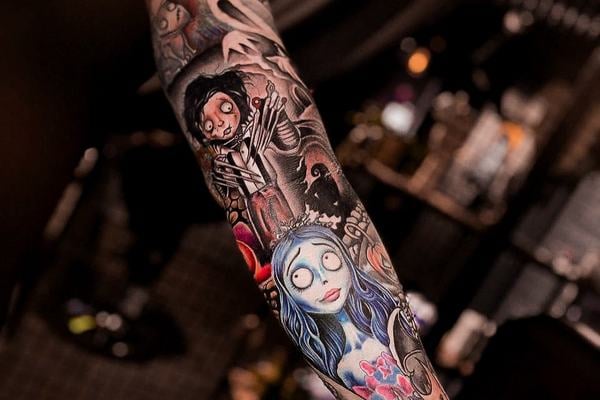 Barevný new school rukáv na mužském předloktí inspirovaný filmem Mrtvá nevěsta (Corpse Bride): modrovlasá nevěsta, kostlivec a duchové; silný kontrast, čisté linky a detailní stínování – ukázka výrazného tetování na ruku vhodného pro větší projekt.