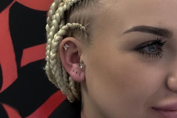Detail pravého ucha s více piercingy (horní helix s malým motýlkem, kroužek ve tvaru srdce na okraji ucha, náušnice v lalůčku); tragus bez šperku – ukázka prostoru a kombinace pro případný tragus piercing.