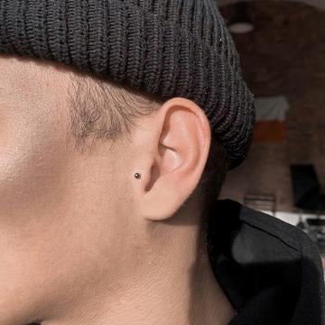 Detail ucha s tragus piercingem – malý, nenápadný labret v chrupavce před vstupem do zvukovodu; příklad decentního umístění a šperku pro počáteční hojení.