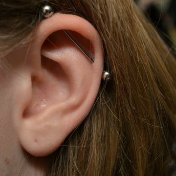 Jemný industrial piercing s jednoduchou činkou v horní části ucha