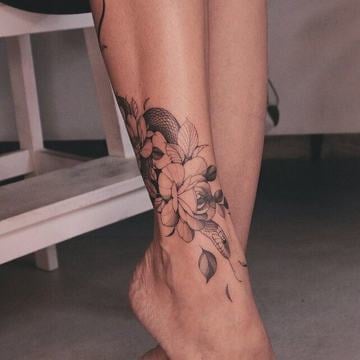 Černobílé linework a dotwork tetování květin a listů na ženském kotníku, které obepíná nohu jako náramek a plynule pokračuje směrem k lýtku.