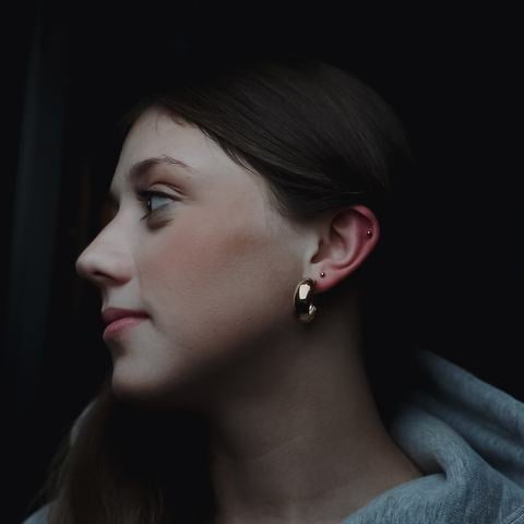 Stylová sestava piercingů v ušním lalůčku kombinuje drobné kovové náušnice s jemným kroužkem. Rozmanité tvary šperků a jejich postupné rozmístění vytvářejí působivý detail s moderním a osobitým charakterem.