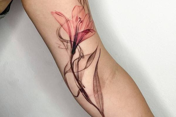 Lilie s růžovými okvětními lístky v akvarel/fine line stylu, protáhlé botanické tetování vedené podél vnitřní paže.