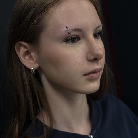 Jemná kombinace piercingu nosního křídla a drobných náušnic v uchu vytváří nenápadné, ale zajímavé zdobení. Stříbrné šperky s minimalistickým designem dodávají vzhledu lehkost a podtrhují přirozené rysy obličeje.