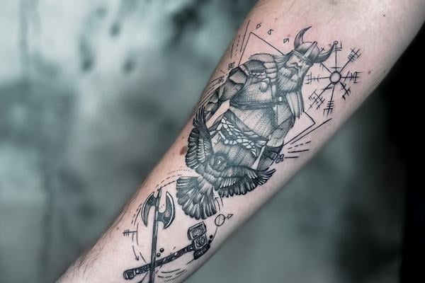 Černošedé pánské tetování na vnitřním předloktí: vikinský bojovník s helmou, havran, sekera a kladivo, kolem runové a severské ochranné symboly v geometrické kompozici; čisté linky a jemné stínování.
