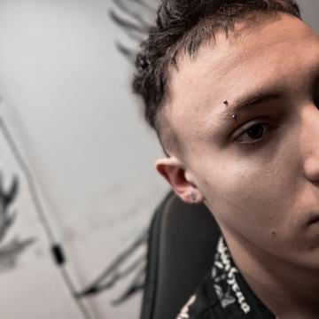 Detail obličeje ve studiu s vertikálním piercingem ve vnější části obočí (zahnutá činka se dvěma kuličkami); ukázka správného umístění a moderního vzhledu piercingu obočí.