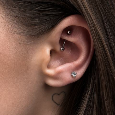 Originální kombinace piercingů ve vnitřní chrupavce ucha s jemným stříbrným kroužkem a drobnými třpytivými kamínky v lalůčku. Rozdílné umístění šperků vytváří zajímavou kompozici, která zvýrazňuje přirozený tvar ucha.