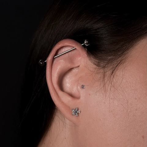Industrial piercing vytváří čistou linii a výrazný detail ucha. Stříbrný šperk působí moderně a sebevědomě.