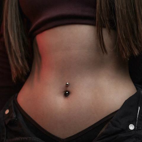 Piercing pupíku působí výrazně a krásně zvýrazňuje siluetu. Tmavý šperk dodává celkovému vzhledu odvážný a moderní charakter.
