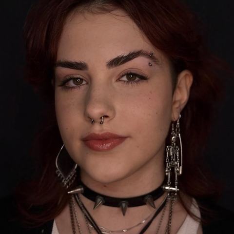 Jemný piercing nosu zvýrazňuje výrazné rysy tváře. Kovový detail přirozeně doplňuje elegantní alternativní styl.
