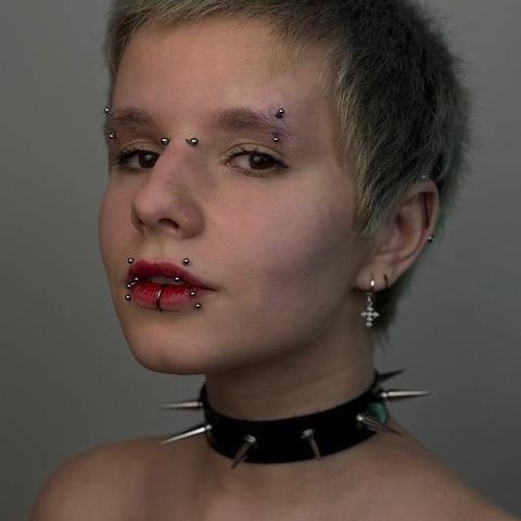Kombinace piercingu obočí a rtů vytváří výrazný, lehce punkový vzhled. Kovové detaily podtrhují osobitý styl a odvážný charakter.