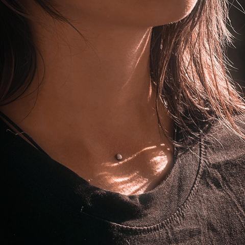 Jemný piercing v oblasti klíční kosti působí jako nenápadný šperk zachycený ve světle. Minimalistický detail krásně zvýrazňuje linii krku a dekoltu.