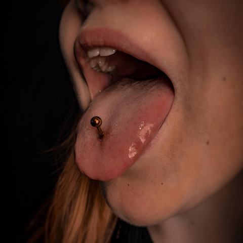 Piercing jazyka dodává úsměvu odvážný a hravý detail. Jemný kovový šperk působí výrazně, ale zároveň přirozeně.
